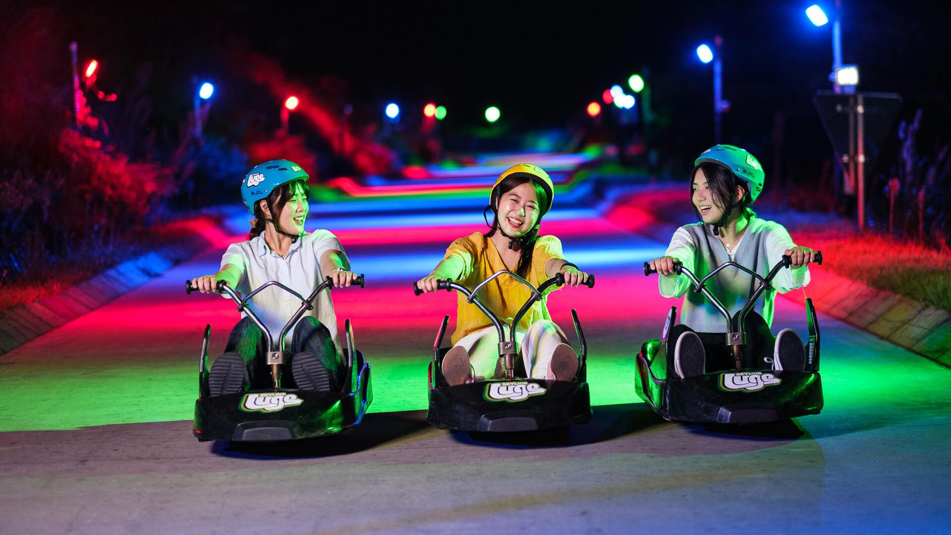 Three ladies smile and laugh as they ride the Night Luge at Skyline Luge Tongyeong.