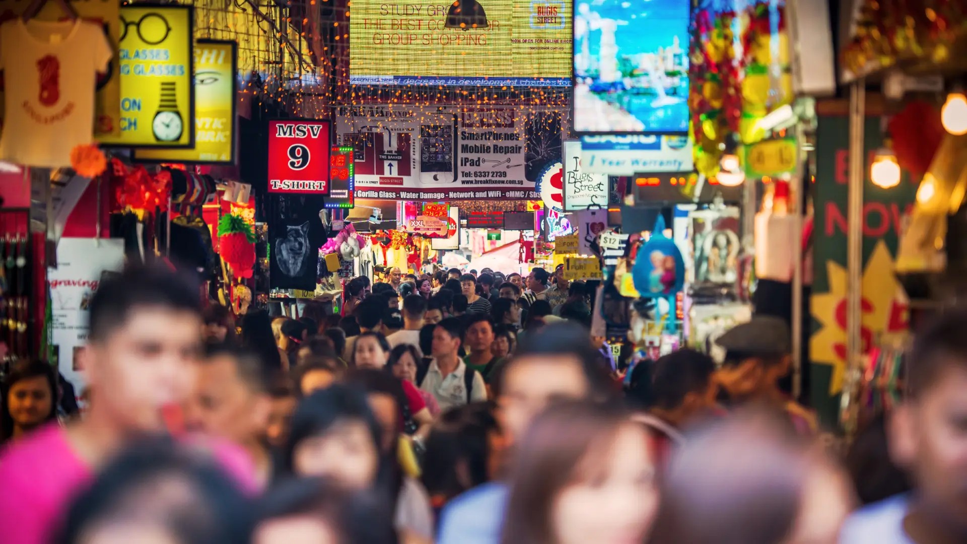 Crowds shopping along Bugis Street Market under bright signs and colourful night lights in Singapore.