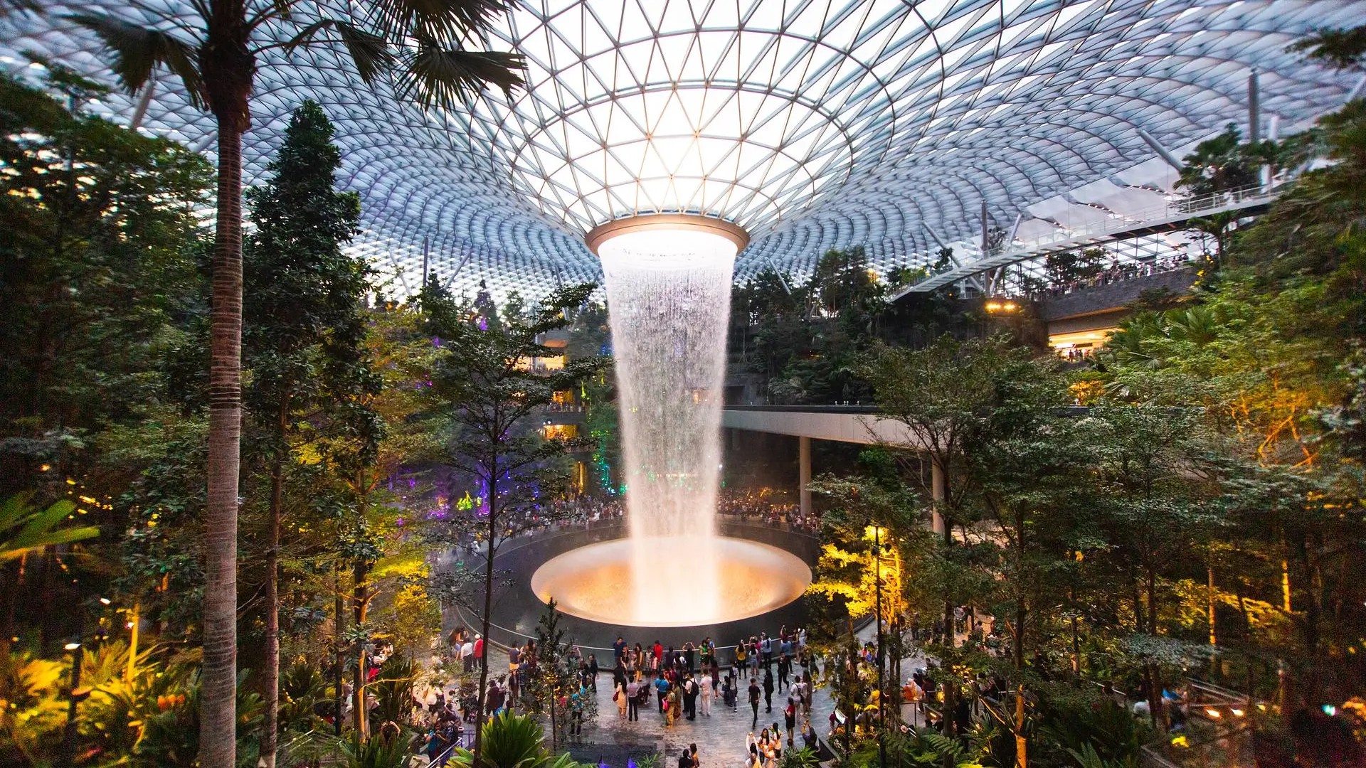 HSBC Rain Vortex waterfall glowing inside Jewel Changi Airport at night.