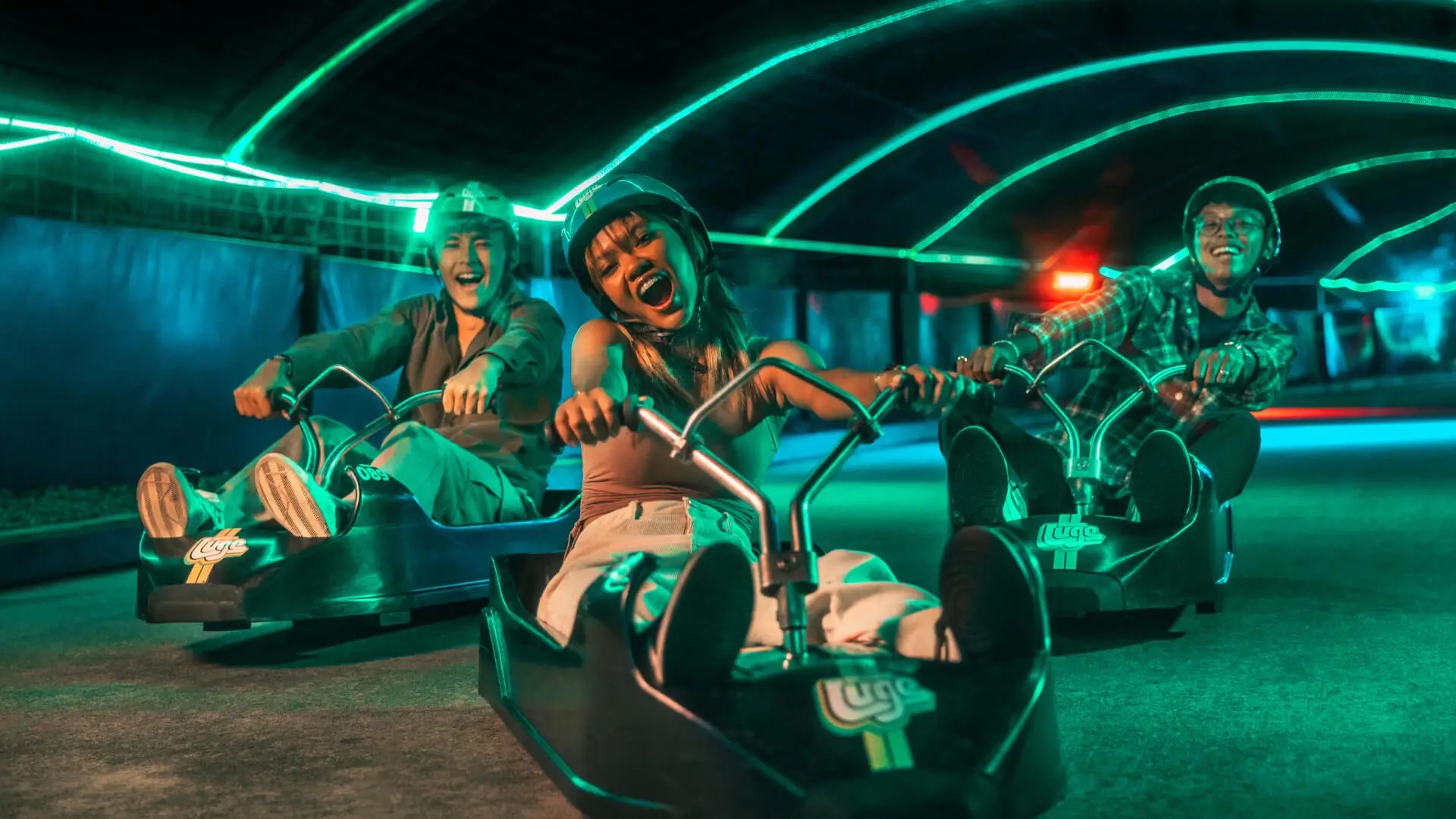 Friends racing under glowing lights on Skyline Luge Sentosa’s night track.