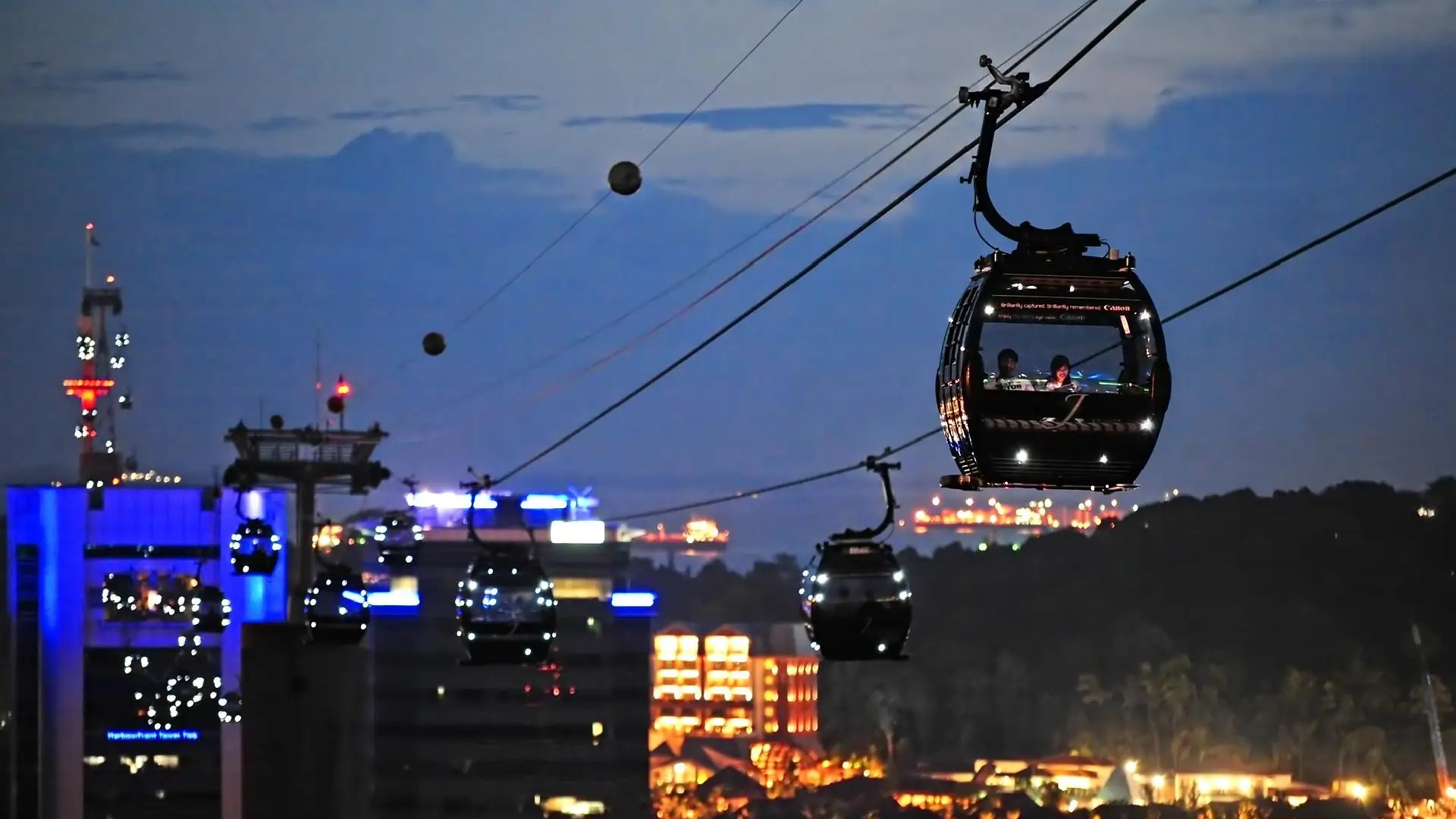 Cable cars gliding over HarbourFront towards Sentosa during a golden Singapore sunset.