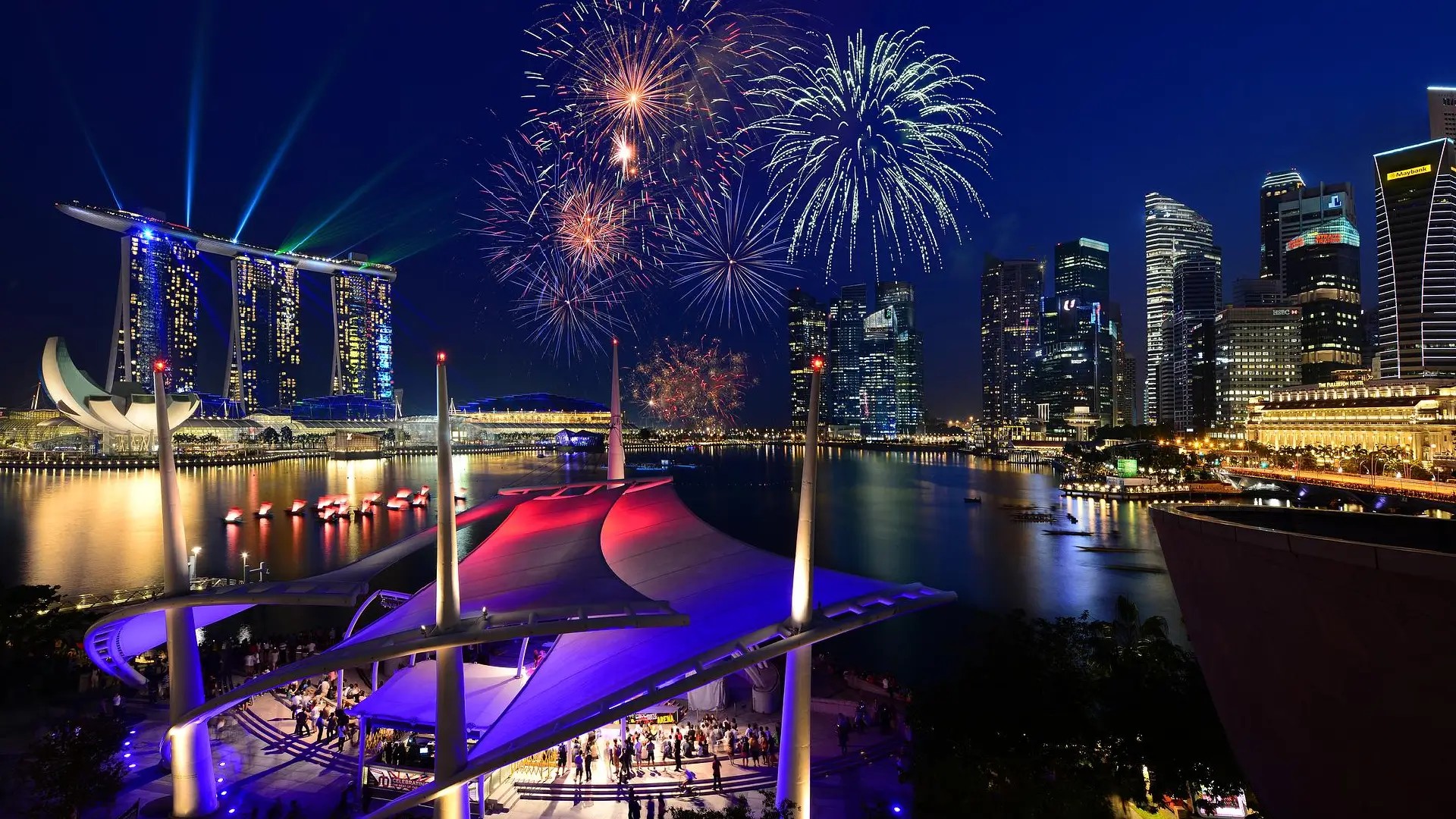 Fireworks over Marina Bay Sands and Singapore skyline reflecting on the water at night.