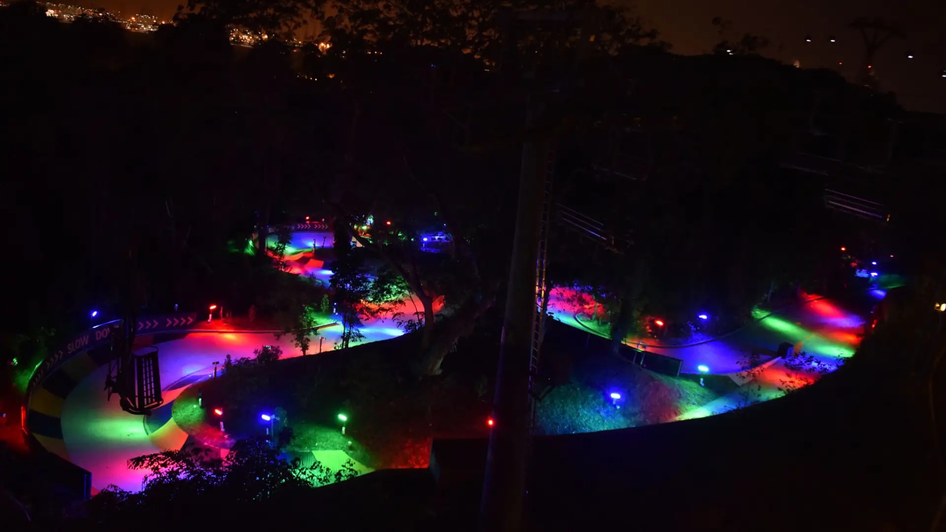 Neon-lit Skyline Luge track at night in Sentosa, Singapore, with colourful lights winding through the forest.