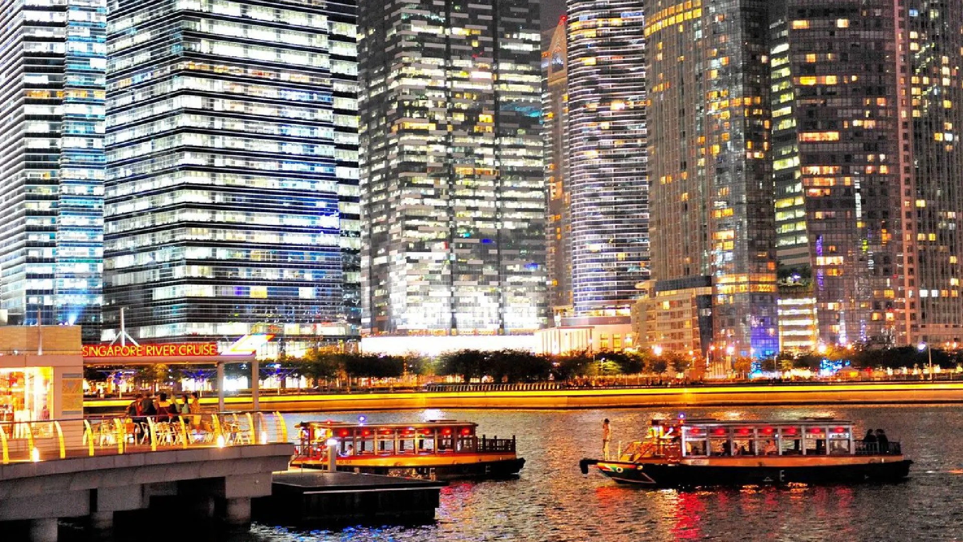 Singapore River Cruise boats passing through Marina Bay at night with illuminated skyscrapers in the background.