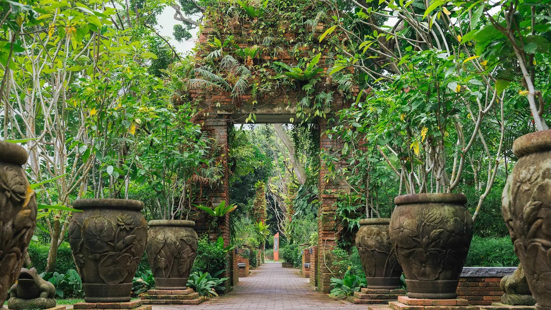 Brick archway covered in lush greenery along a landscaped pathway in Fort Canning Park, Singapore.