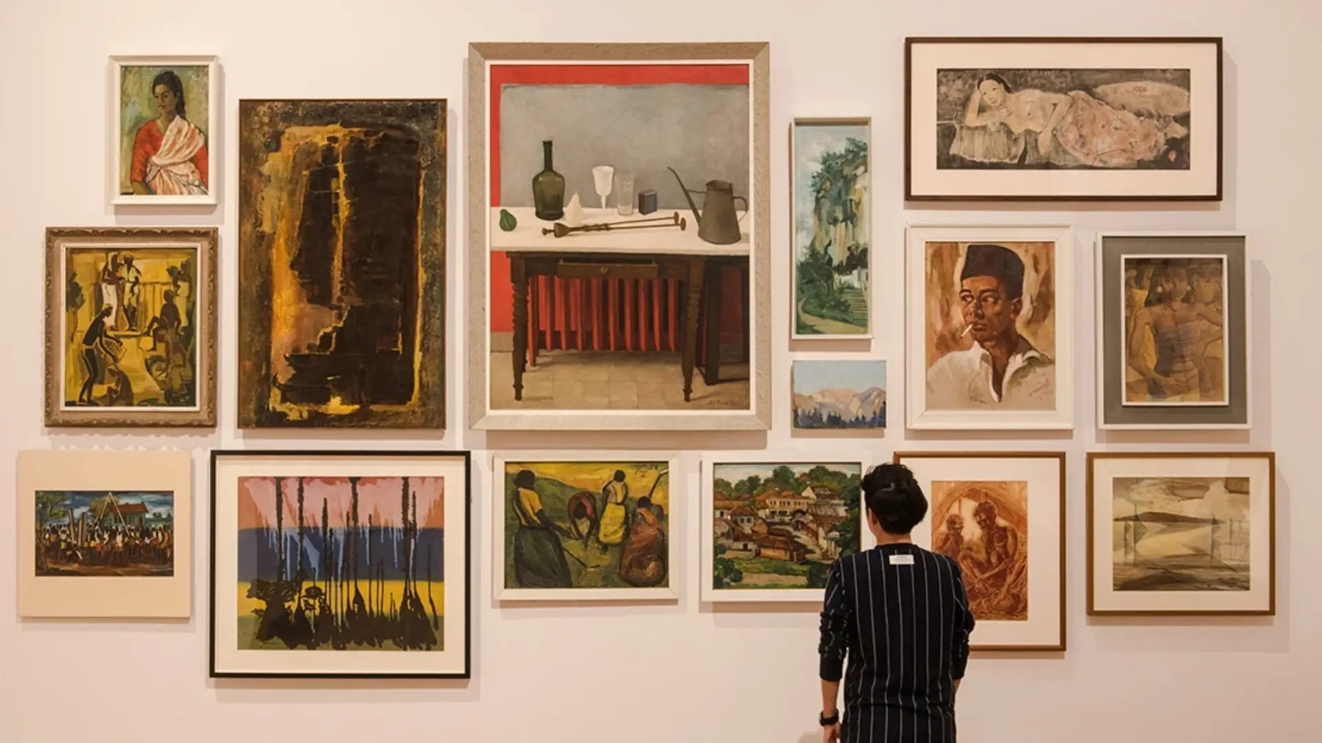 Visitor standing in front of a gallery wall filled with Southeast Asian paintings at the National Gallery Singapore.