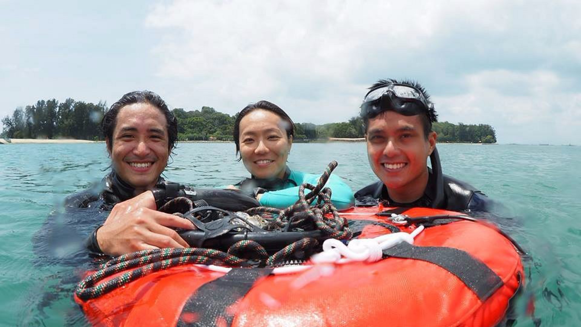 Three freediving instructors smiling in the water during a training session off the coast of Singapore.