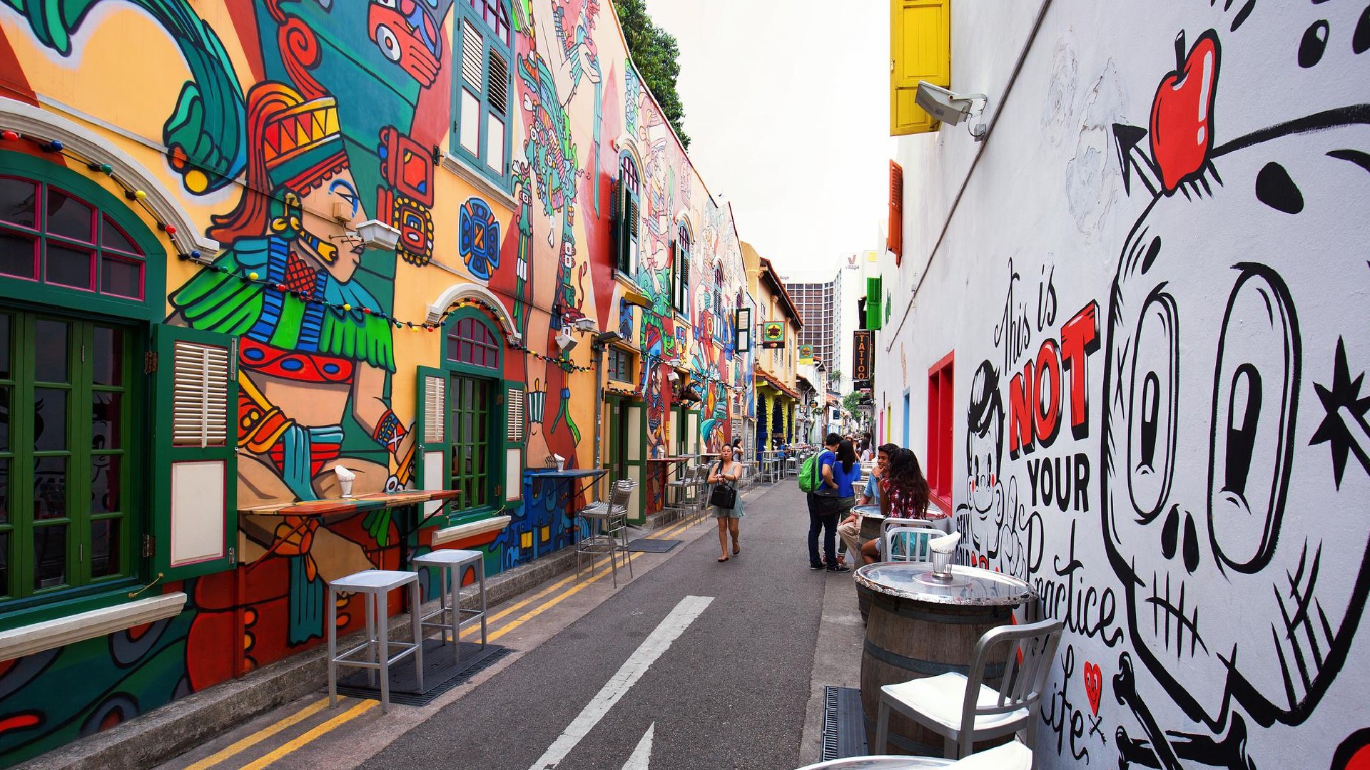 Colourful street art and mural-covered shophouses along Haji Lane in Singapore, with people walking and outdoor seating.