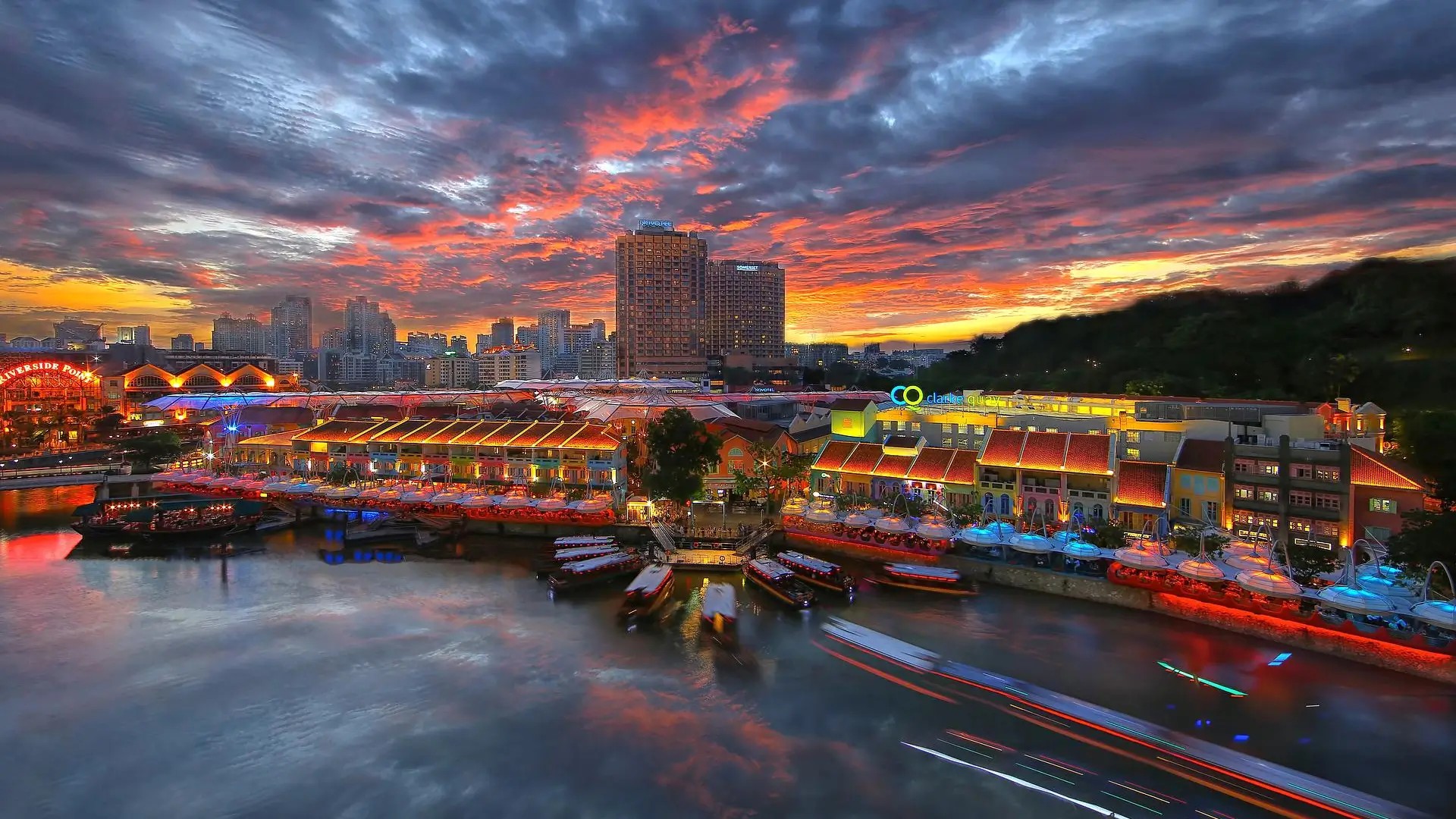 Sunset view of Clarke Quay in Singapore with colourful riverside shophouses, night lights and boats along the Singapore River.
