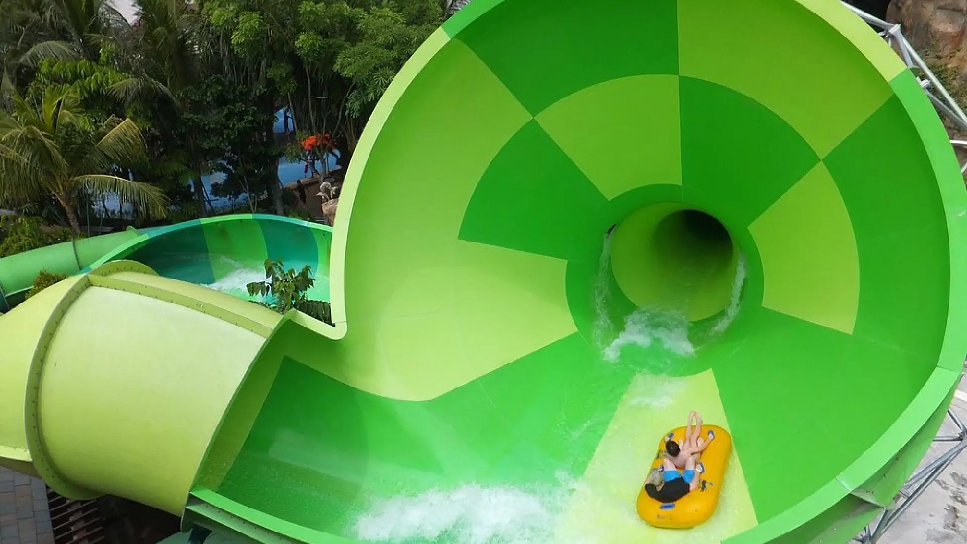 Visitors sliding down a bright green water slide at Adventure Cove Waterpark Singapore.