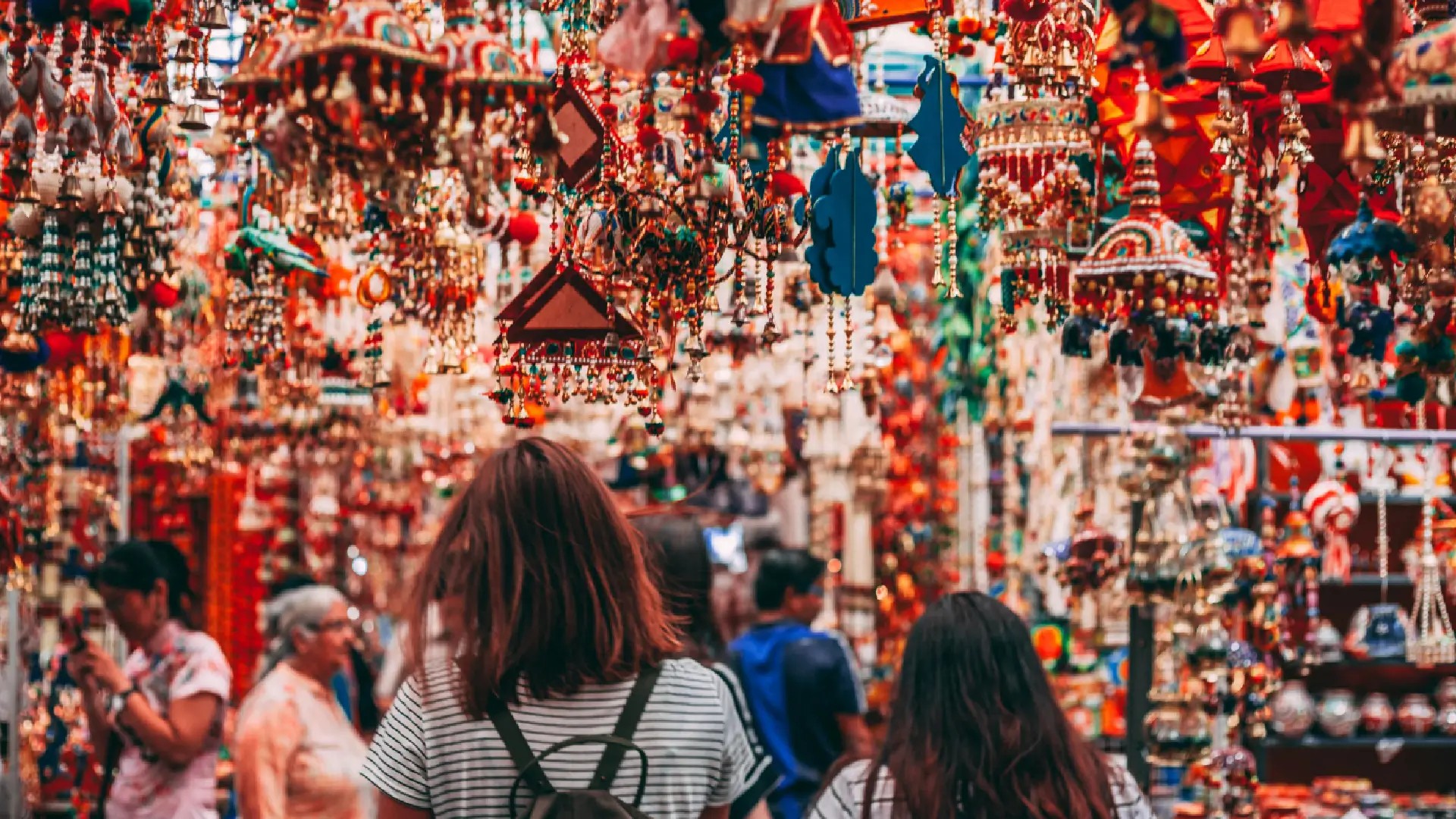 Visitors exploring vibrant hanging decorations at a colourful market in Little India Singapore.
