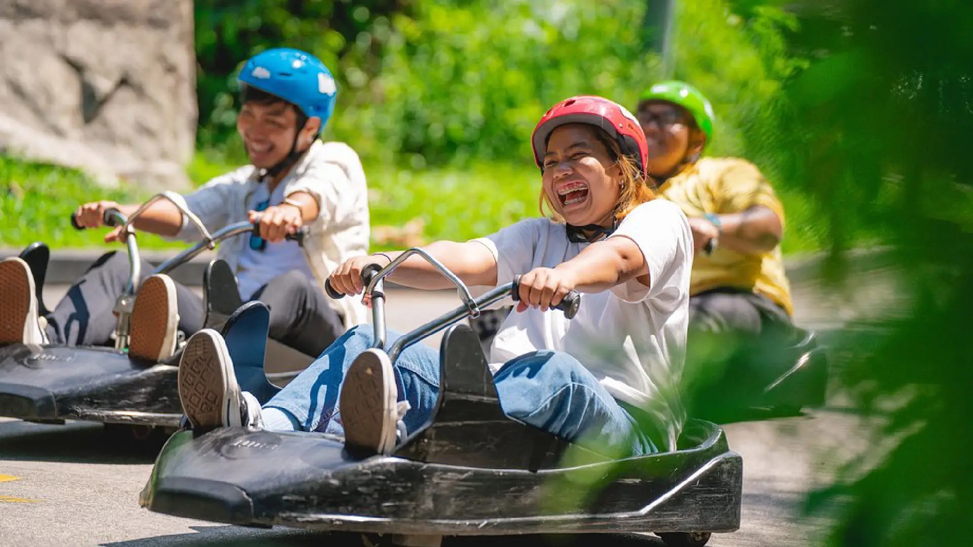 Friends riding luges down the track at Skyline Luge Singapore on a sunny day.