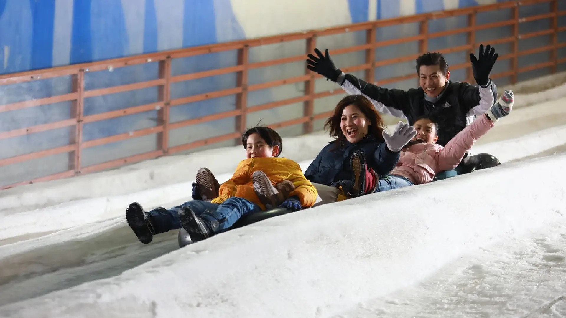 Family sledding together at Snow City Singapore, enjoying the indoor winter playground and snowy slides.