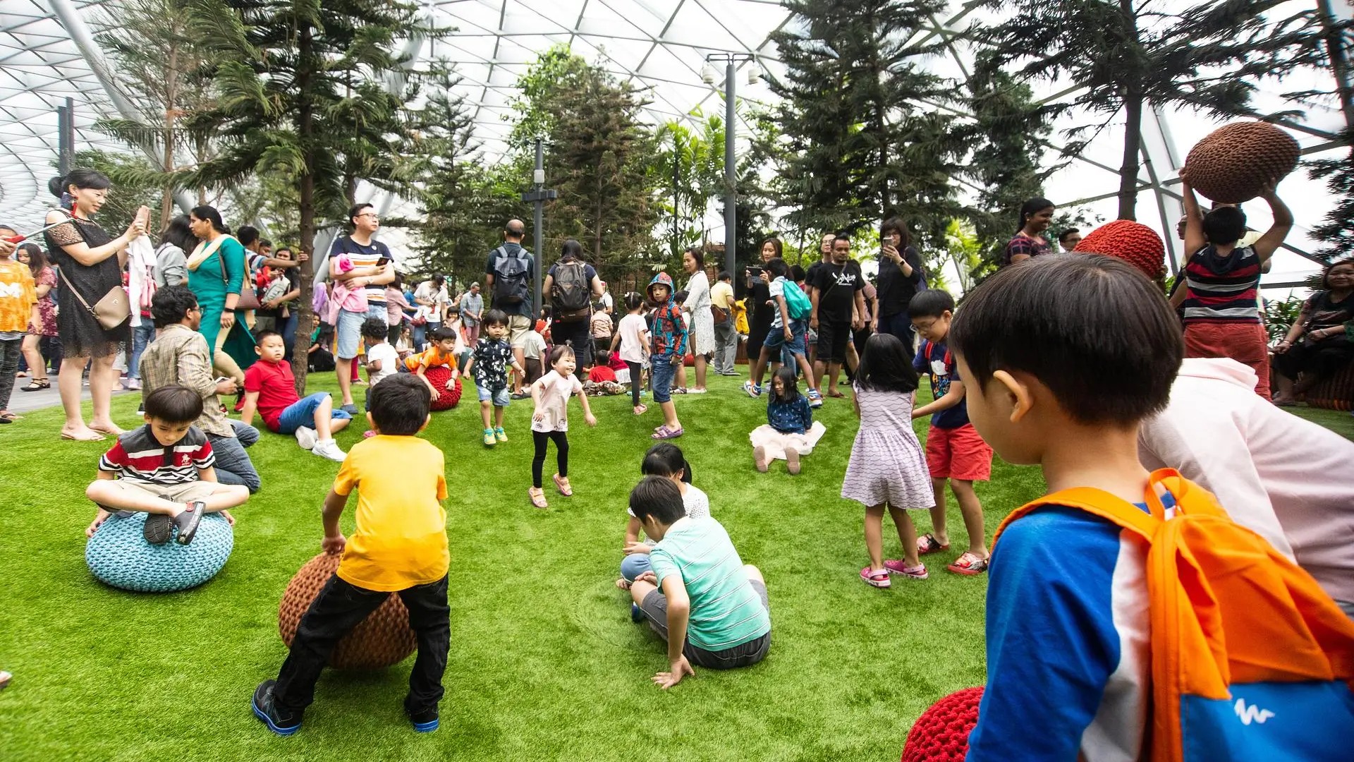 Children playing and families gathered at the indoor garden play area in Canopy Park, Jewel Changi Singapore, under the glass-domed roof.