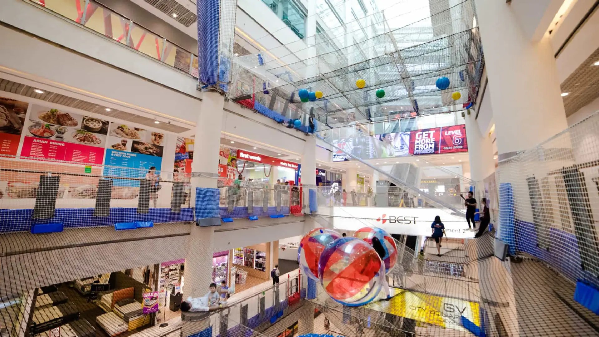 Indoor suspended nets playground at AIRZONE in Singapore, with colourful balls and people playing across multiple mall levels.