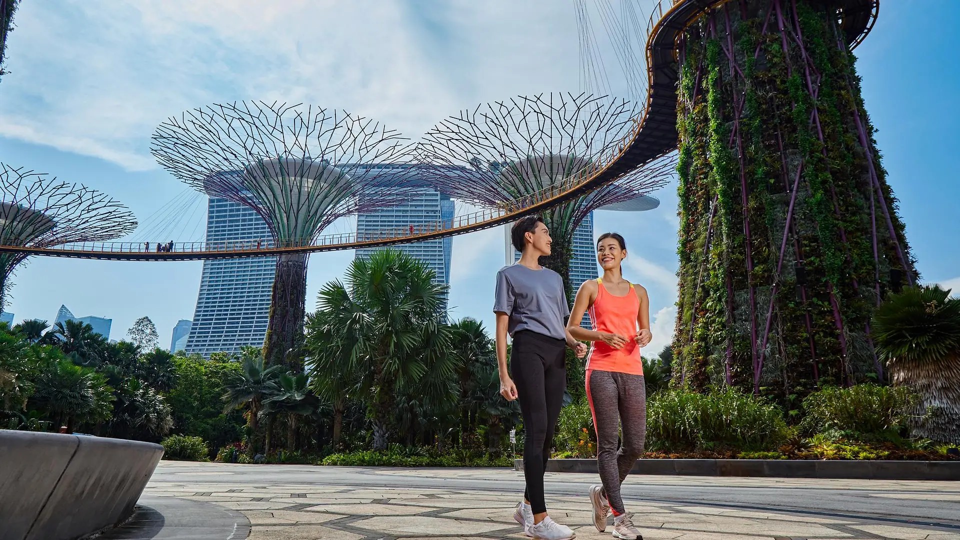 Couple walking beneath the Supertree Grove at Gardens by the Bay in Singapore, with skyline views in the background.