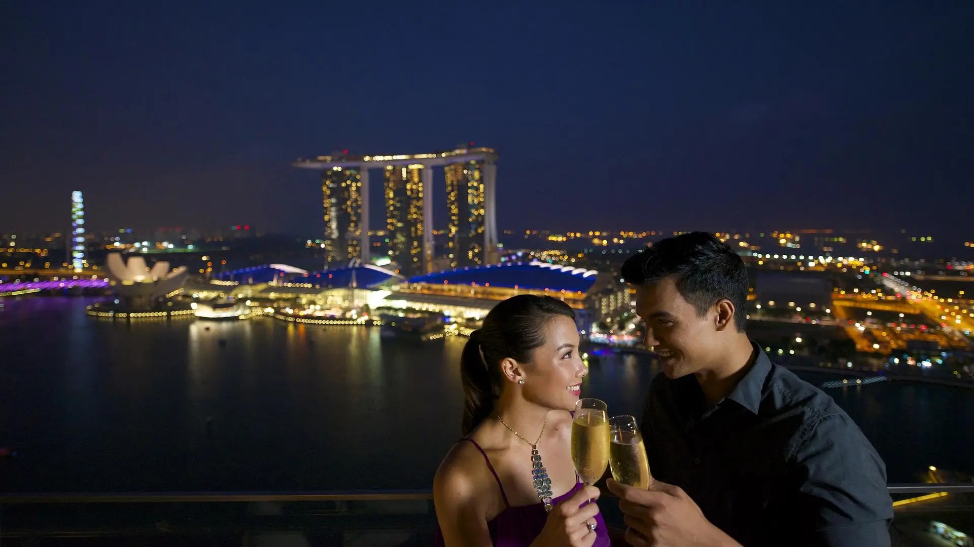 Couple enjoying champagne with panoramic night views of Marina Bay Sands and the Singapore skyline in the background.