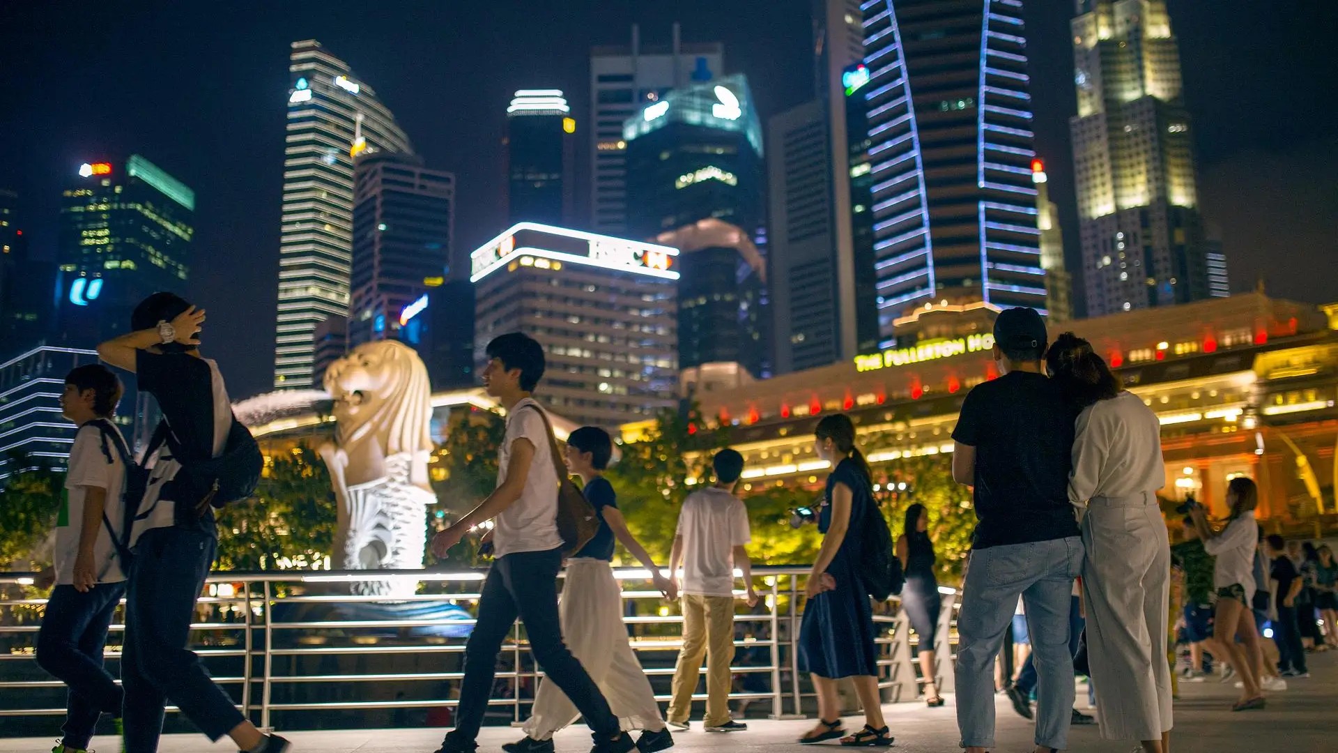 Couple enjoying the night skyline at Merlion Park in Singapore, surrounded by city lights and waterfront views.