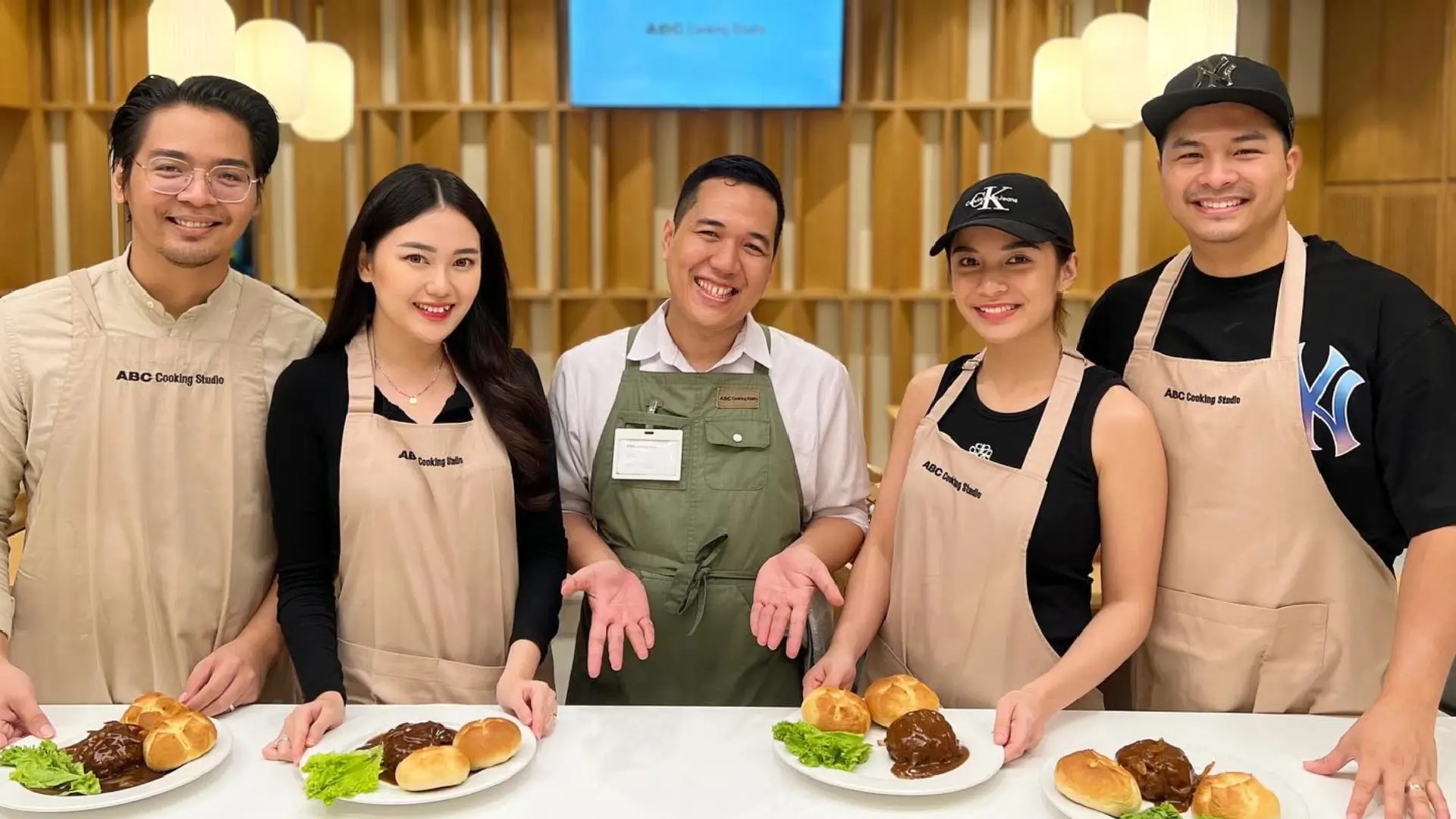 A group in aprons presenting their finished dishes at ABC Cooking Studio in Singapore during a fun, hands-on cooking class.