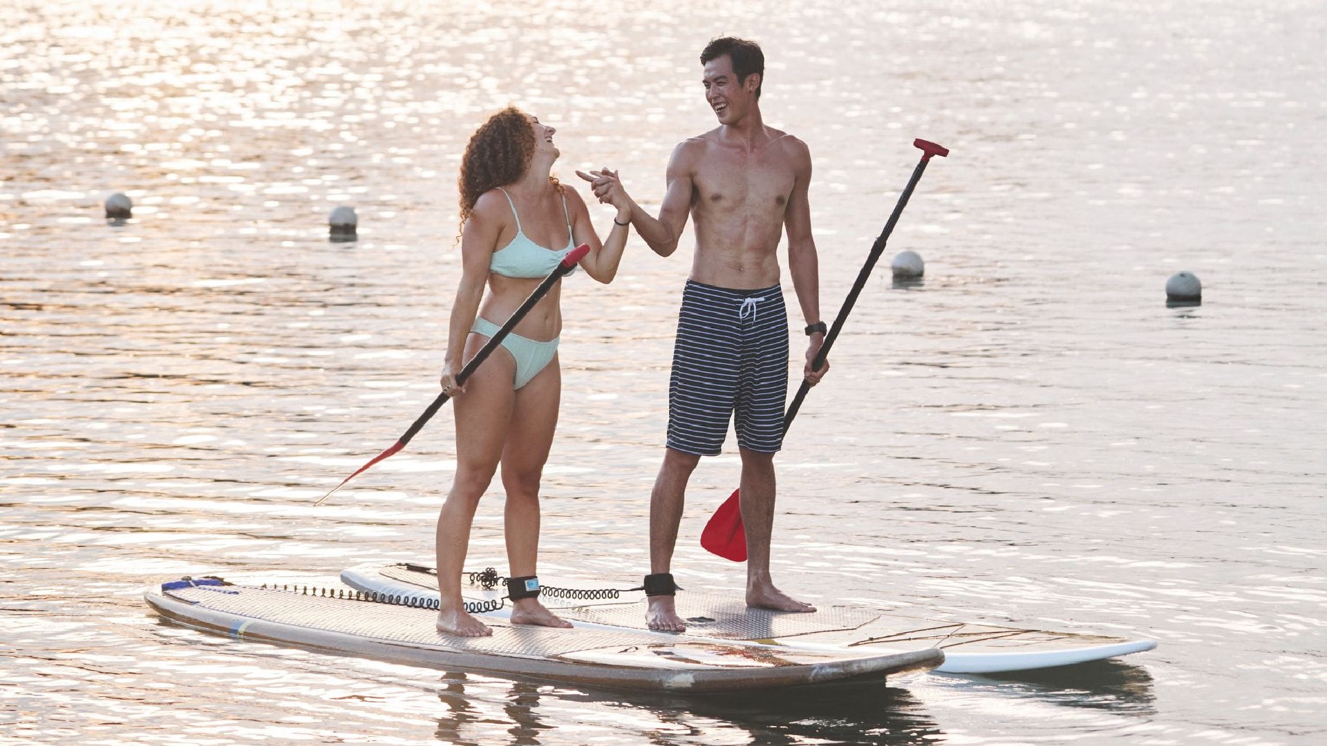 Couple stand-up paddleboarding at Ola Beach Club on Sentosa Island, enjoying a popular water sport in Singapore.