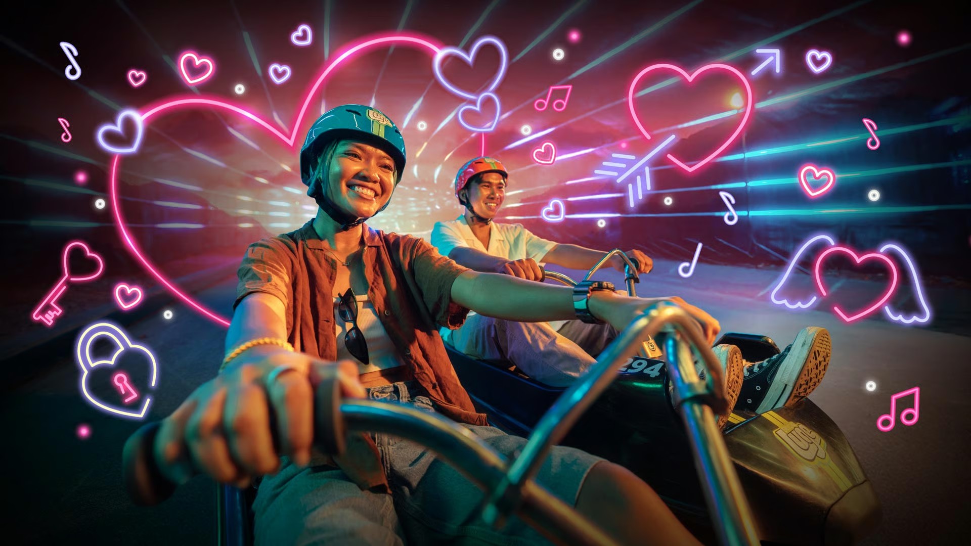 Couple enjoying a romantic Night Luge ride at Skyline Luge Singapore, with vibrant neon heart graphics surrounding them.