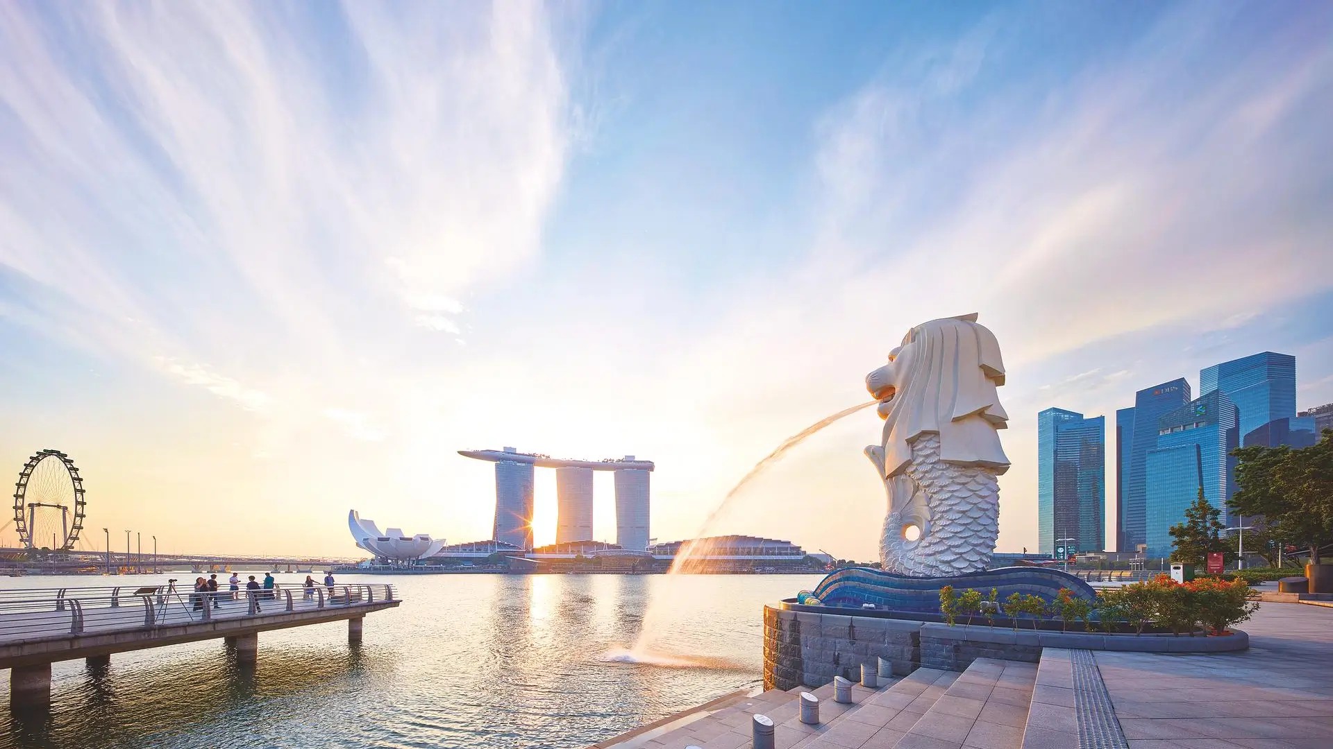 The Merlion statue at sunrise in Merlion Park, with Marina Bay Sands and Singapore’s skyline reflected on the water.