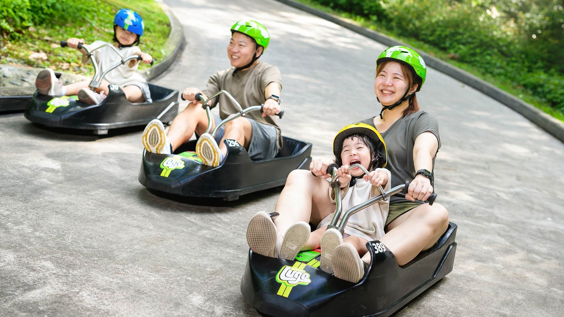 Family enjoying a tandem ride at Skyline Luge Singapore, with parents and children riding luge carts downhill.