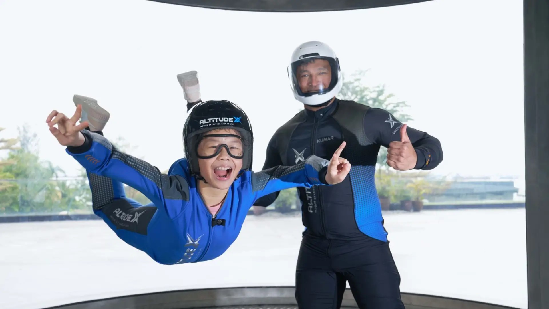 Child enjoying indoor skydiving at AltitudeX Singapore, floating in a wind tunnel with an instructor nearby.