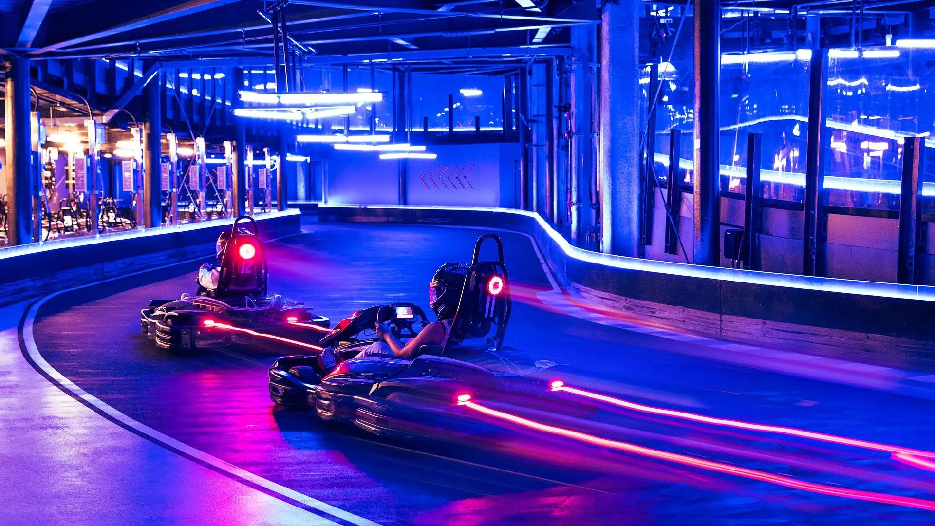 Riders racing neon-lit go-karts at HyperDrive Sentosa, a futuristic indoor track combining real-world go-karting with virtual gaming effects.