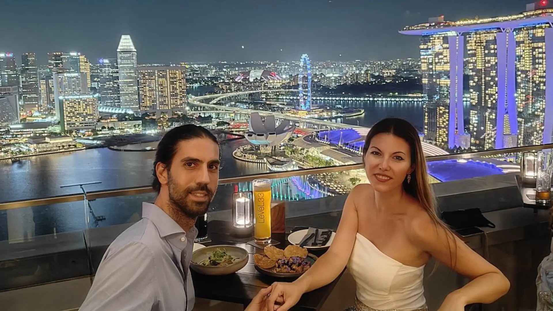 Couple enjoying rooftop sunset cocktails with panoramic Singapore skyline views at a city rooftop bar overlooking Marina Bay