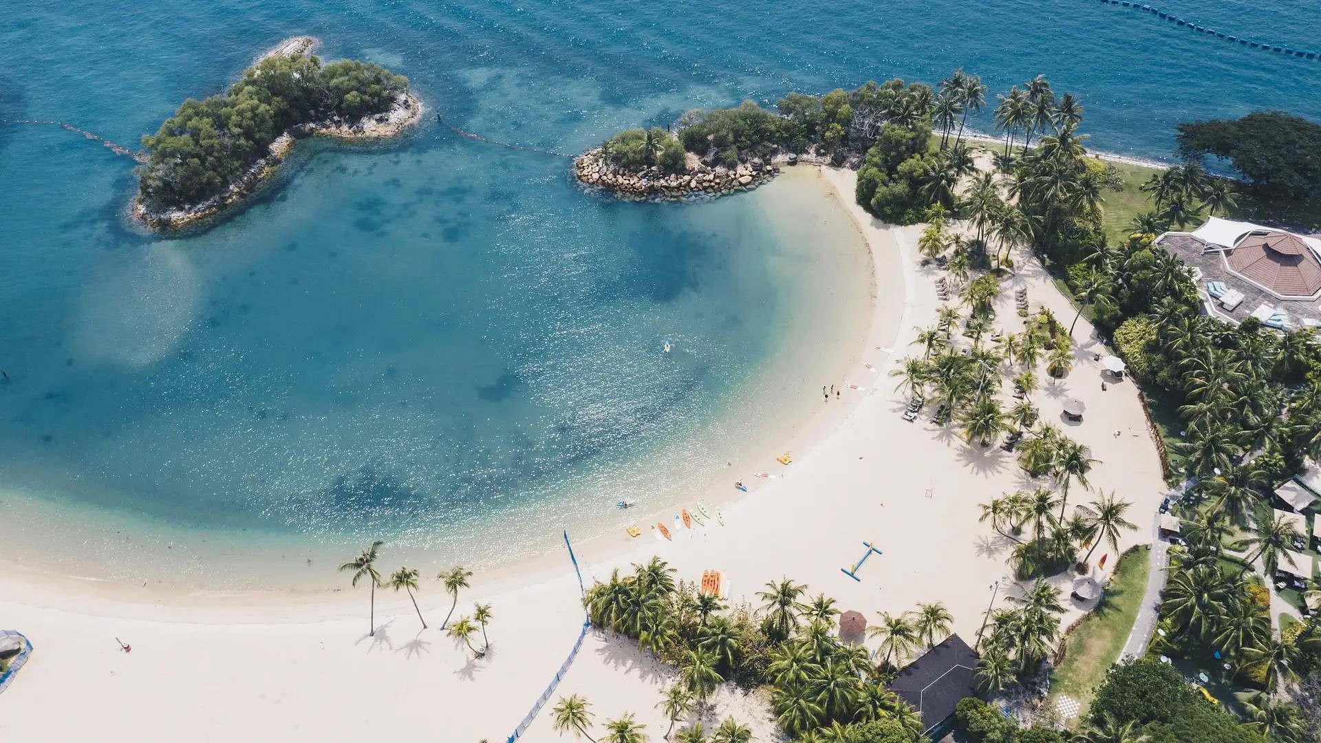 Aerial view of Sentosa Island beach with turquoise water, white sand, palm trees, and people enjoying beach activities