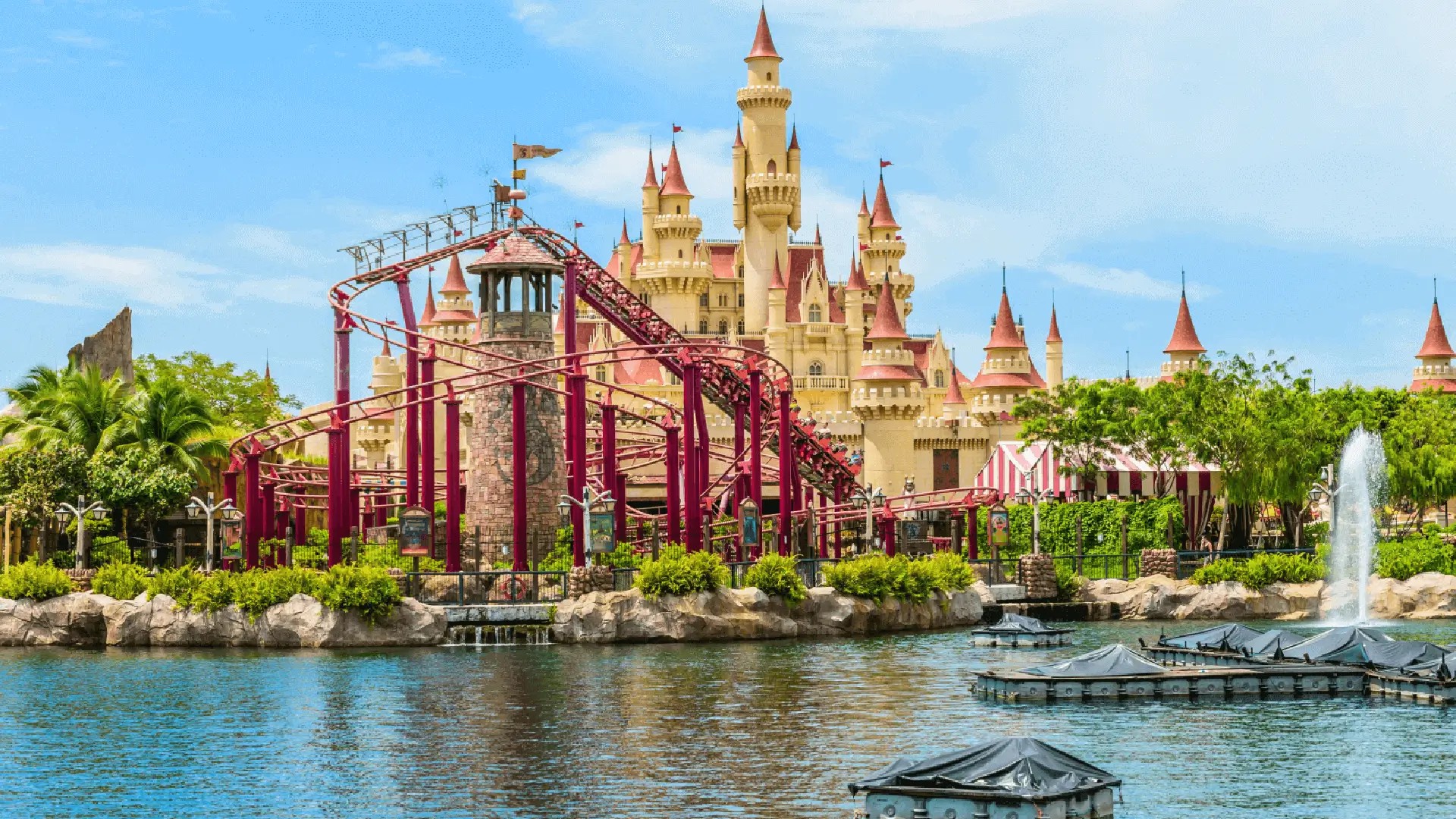 Universal Studios Singapore with castle backdrop, roller coaster tracks, lagoon water and lush greenery under a bright blue sky