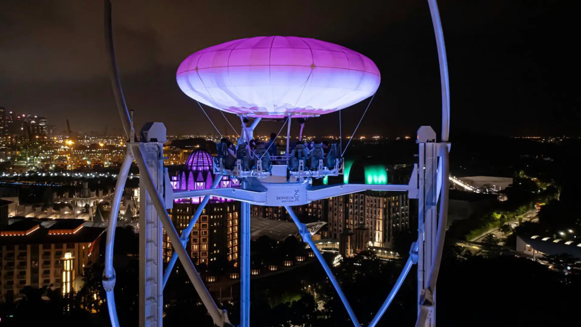 Open-air SkyHelix Sentosa ride glowing at night, lifting riders above Singapore’s skyline with panoramic harbour views