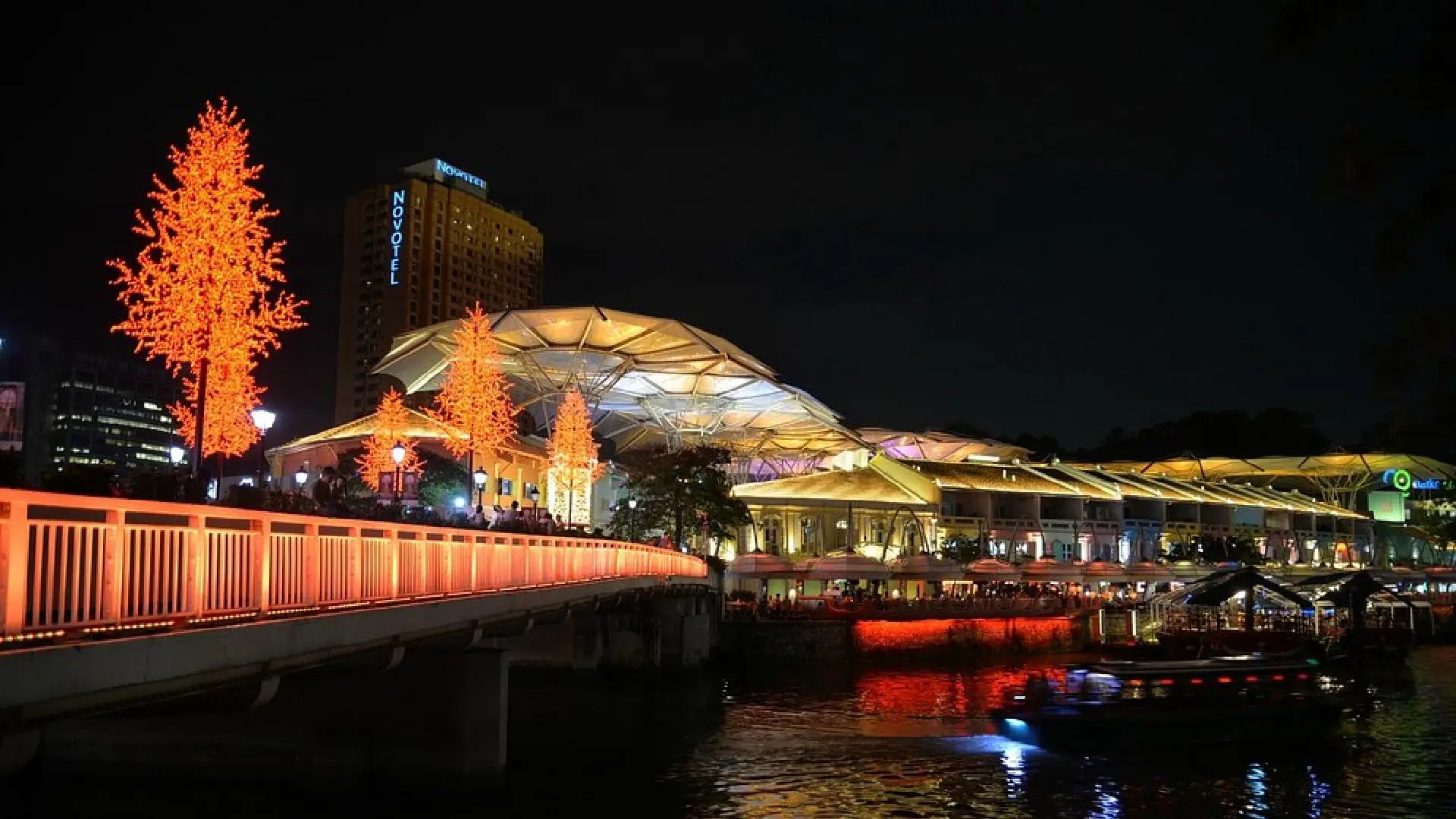 Clarke Quay at night with illuminated riverside bars, bridges, and boats reflecting colourful lights on the Singapore River.