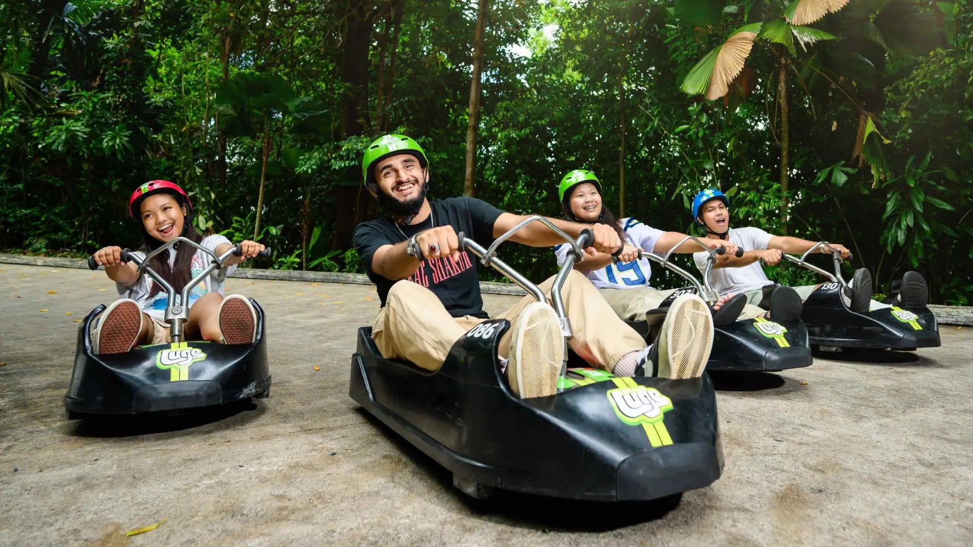 Friends enjoying a Skyline Luge ride in Sentosa, racing downhill through tropical jungle tracks in Singapore.