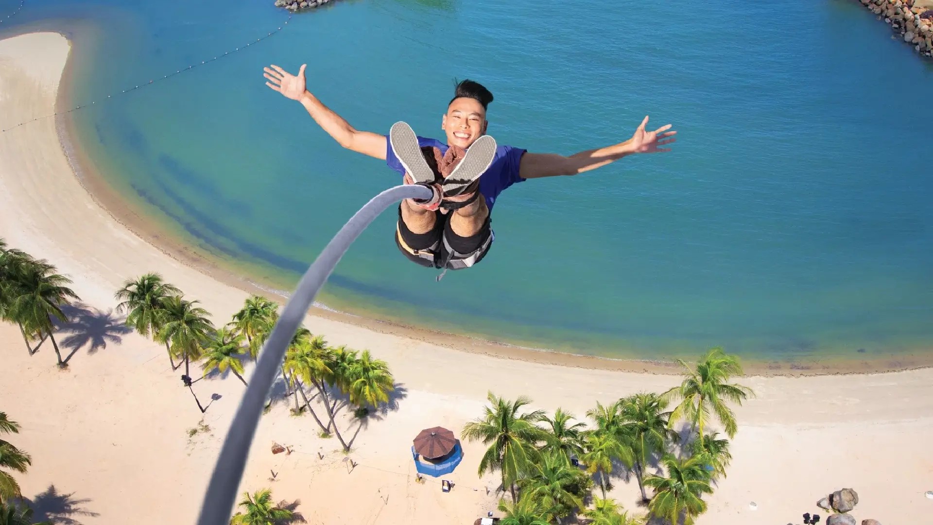 Person bungy jumping at AJ Hackett Sentosa above Siloso Beach with ocean and palm trees below