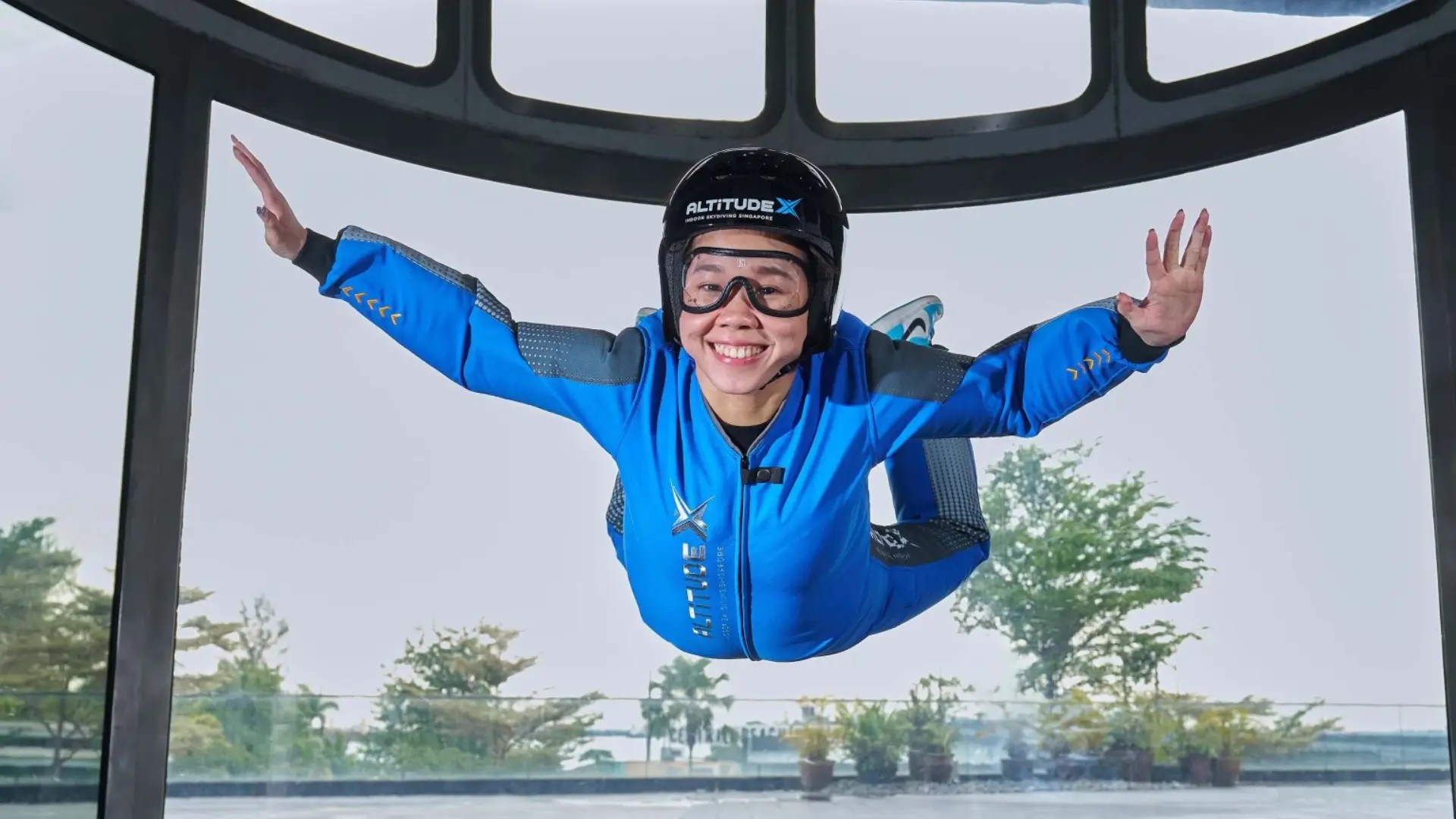 Person indoor skydiving at AltitudeX Singapore, floating in a vertical wind tunnel with instructor guidance