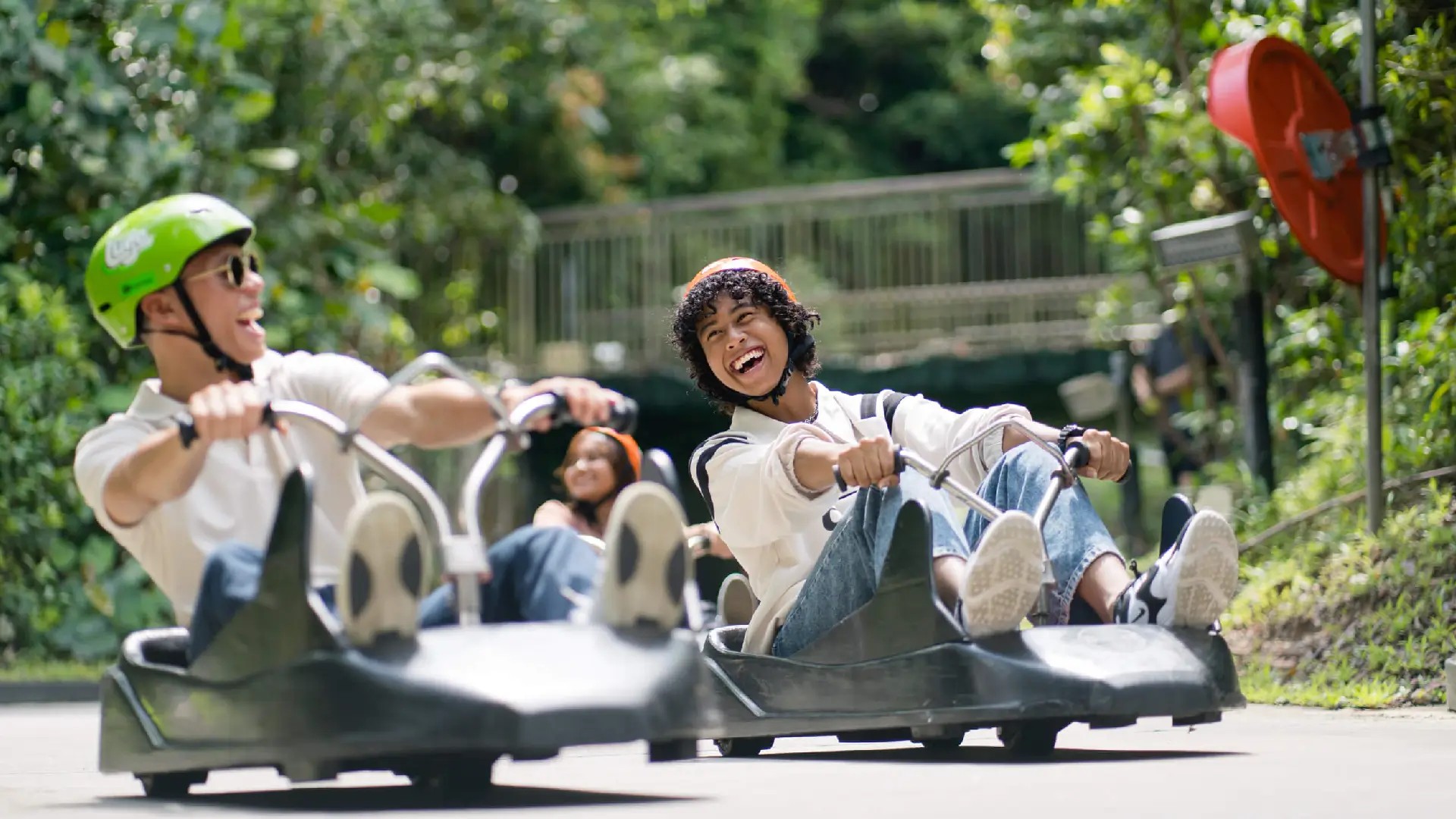 Friends riding the Skyline Luge Singapore track and smiling during the downhill luge experience