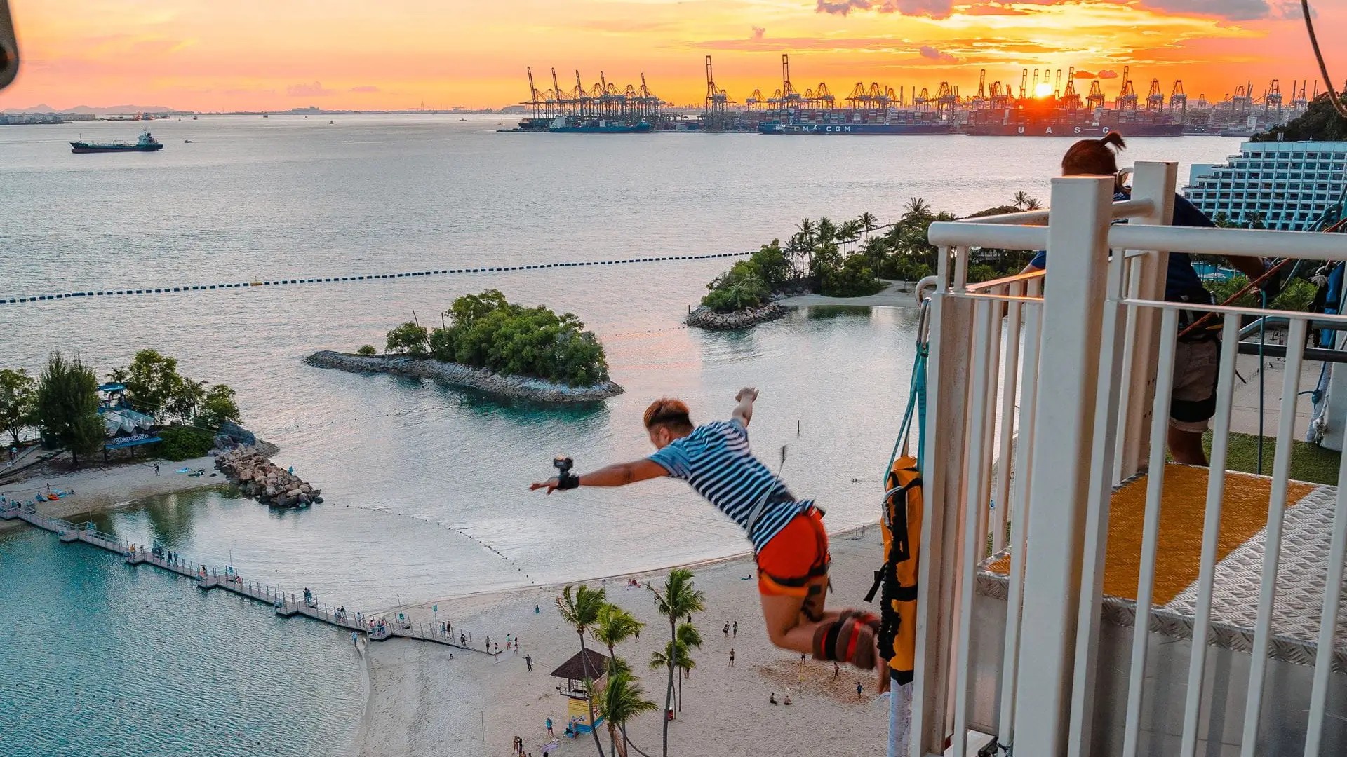 Person bungy jumping at AJ Hackett Sentosa with sunset views over Siloso Beach and Singapore harbour