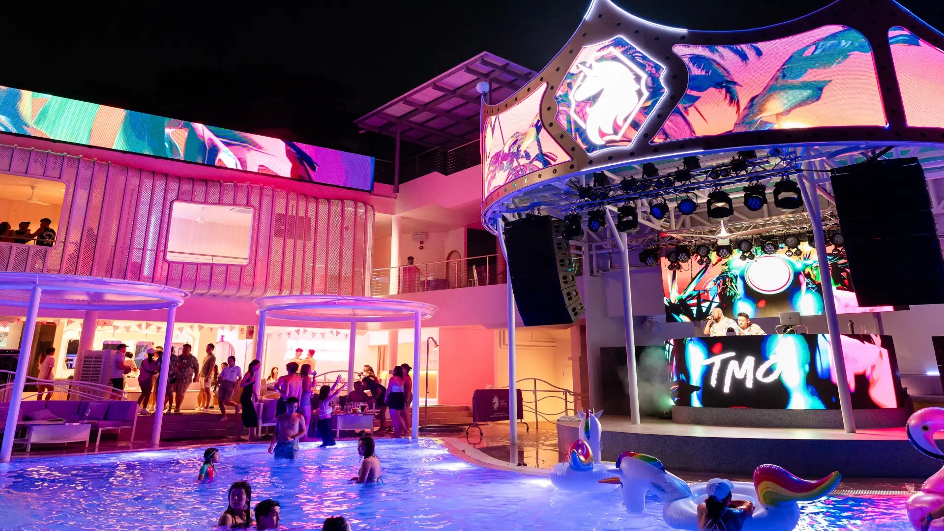 Nighttime pool party at a Sentosa beach club with DJ stage, colourful lights, and people relaxing in the water
