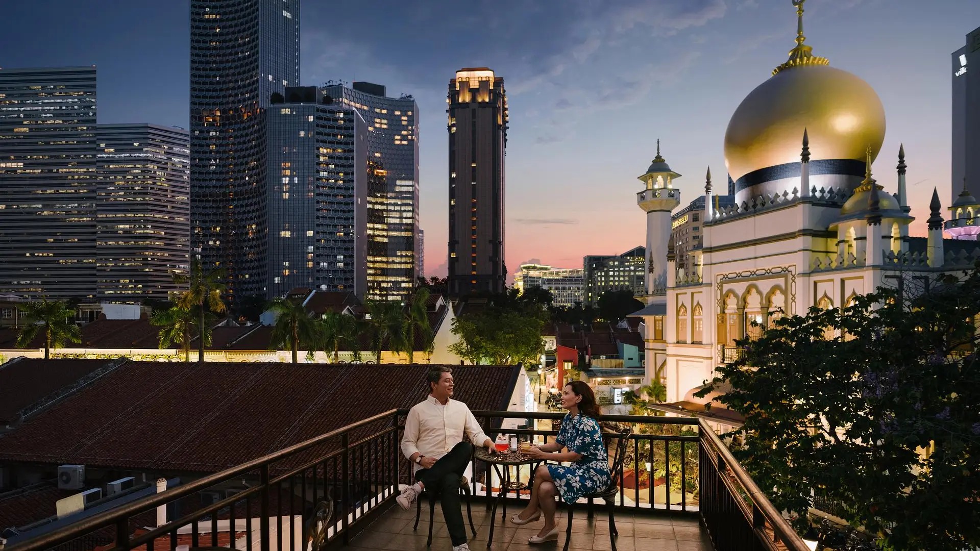 Couple enjoying a romantic evening drink on a balcony with Singapore city skyline and mosque views at dusk