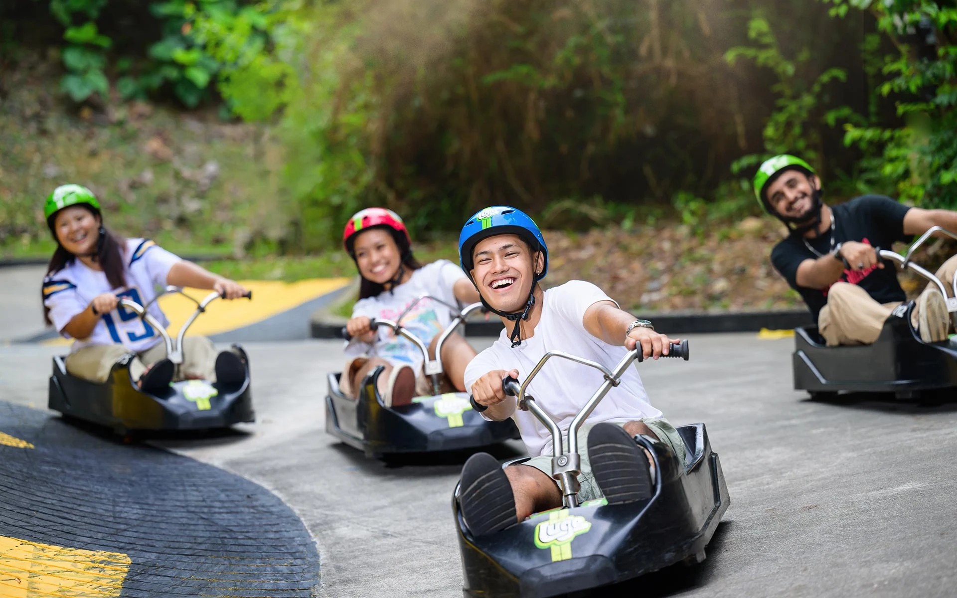 Group of friends riding Skyline Luge carts together, smiling as they race down a curved outdoor track.