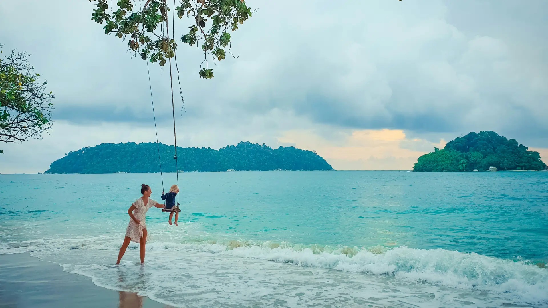 Tree swing on a tropical beach overlooking turquoise water and small islands.