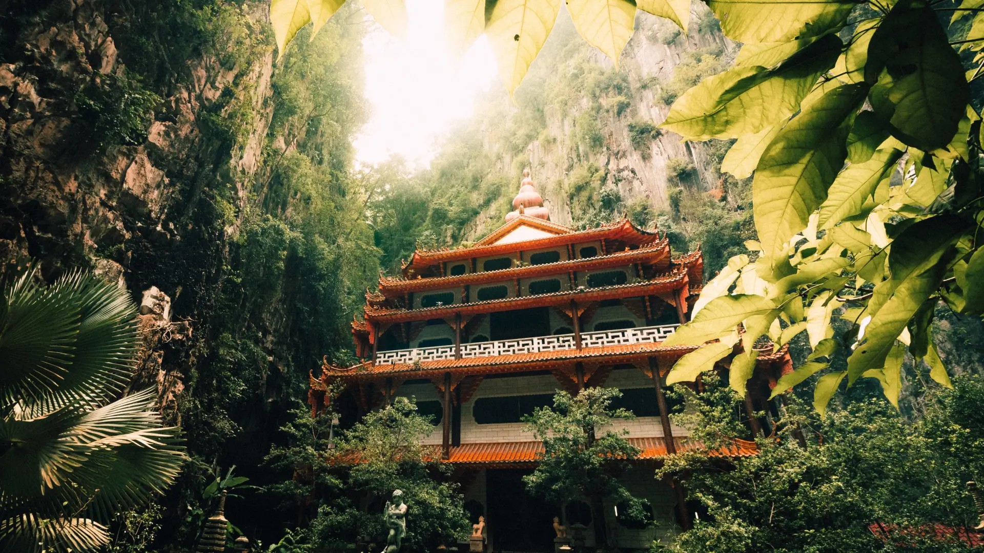 Traditional temple nestled within a limestone cave surrounded by tropical vegetation in Perak, Malaysia.