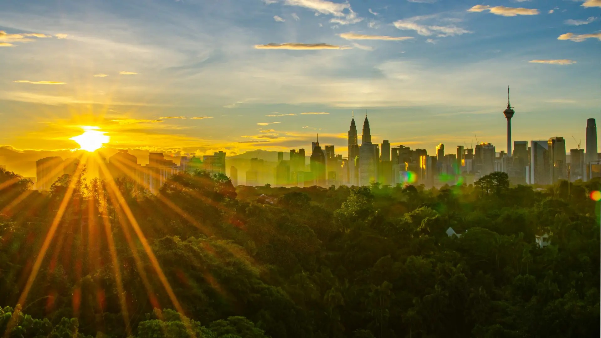 Sunrise over the Kuala Lumpur skyline, featuring the Petronas Twin Towers and KL Tower above lush green parkland in Malaysia.