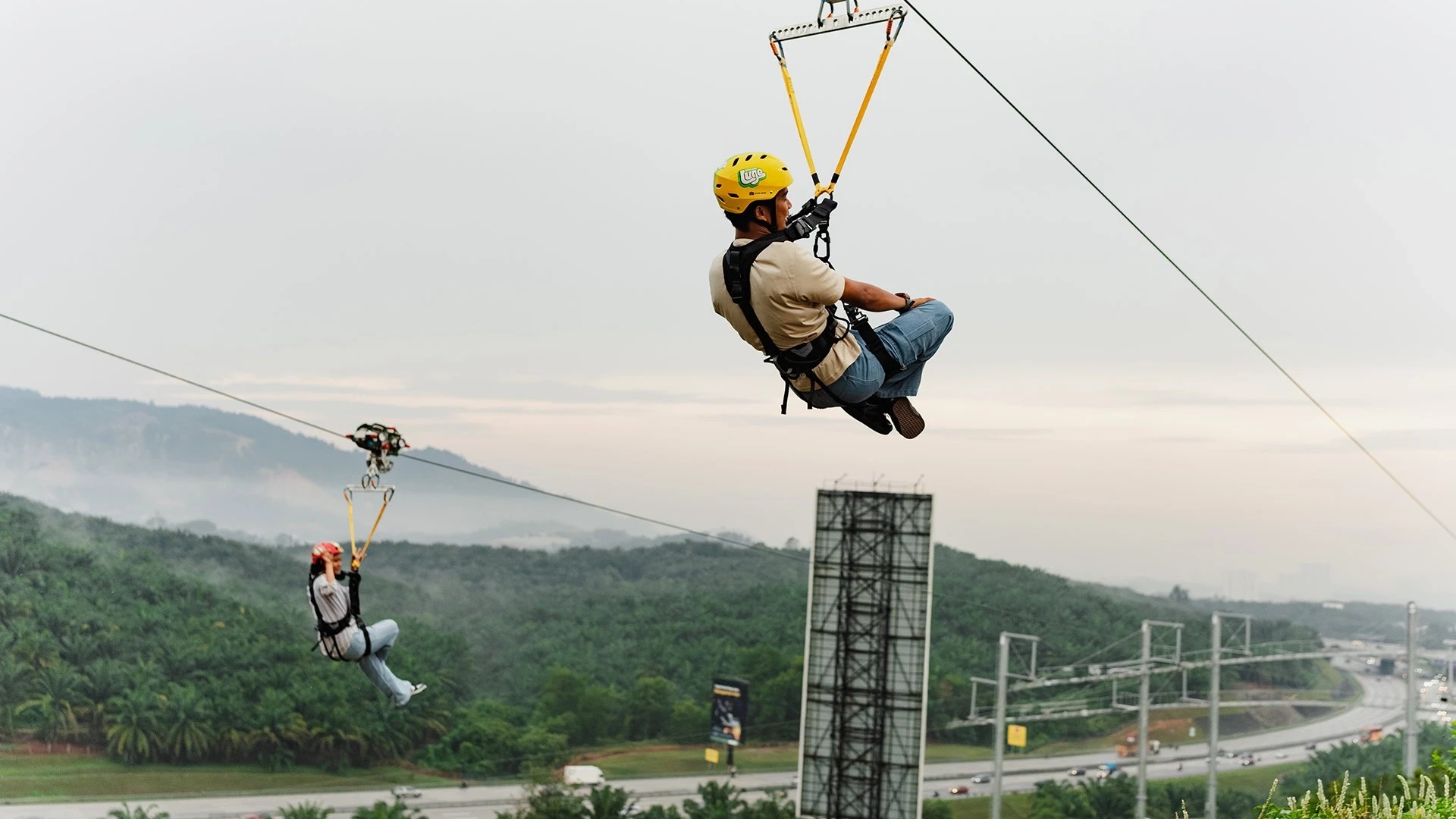 Visitors riding the HyFly Zipline at Skyline Luge Kuala Lumpur with views of the surrounding hills