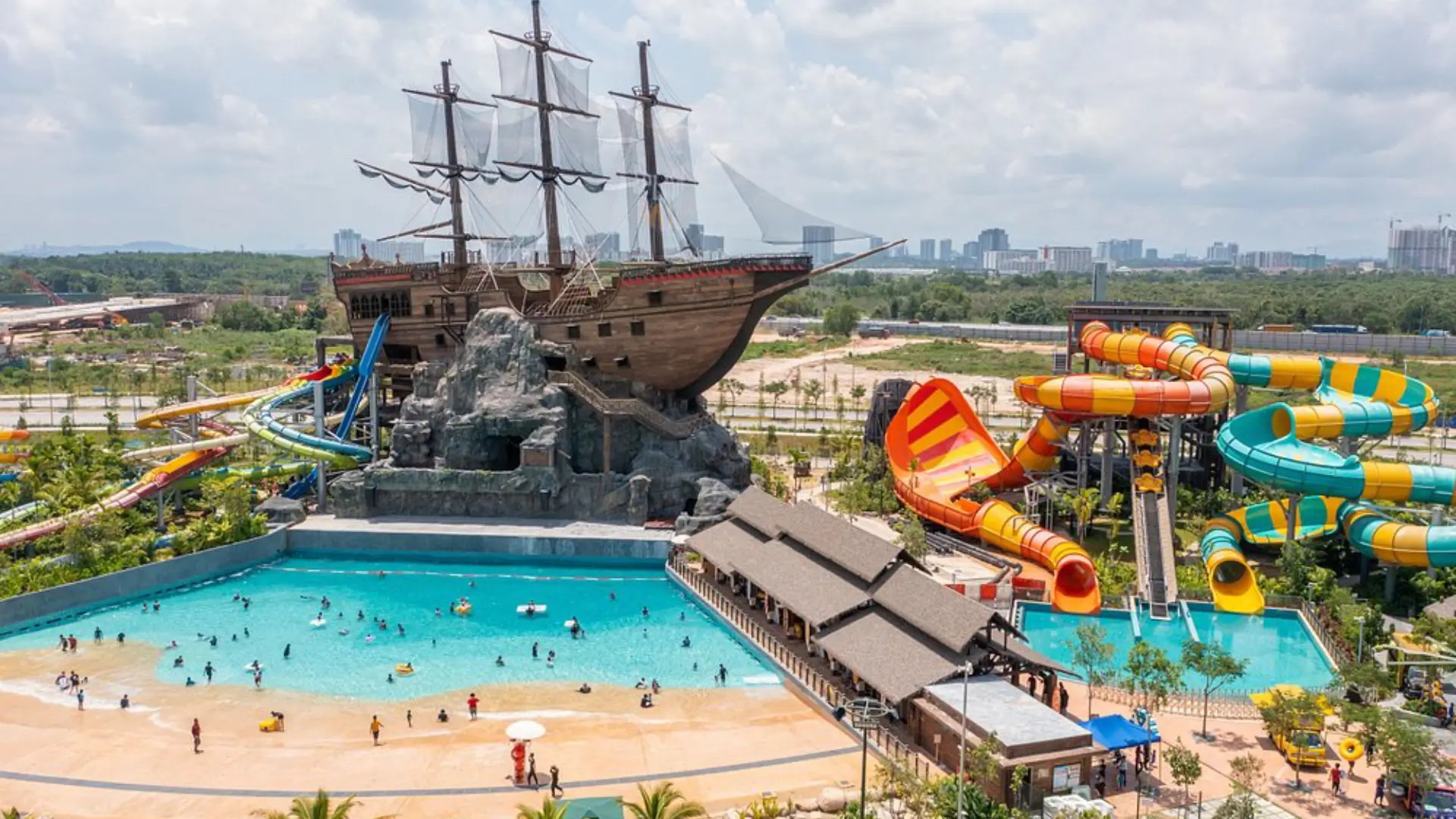 Aerial view of SplashMania WaterPark at Gamuda Cove, featuring a large pirate ship, swimming pool and colourful waterslides.